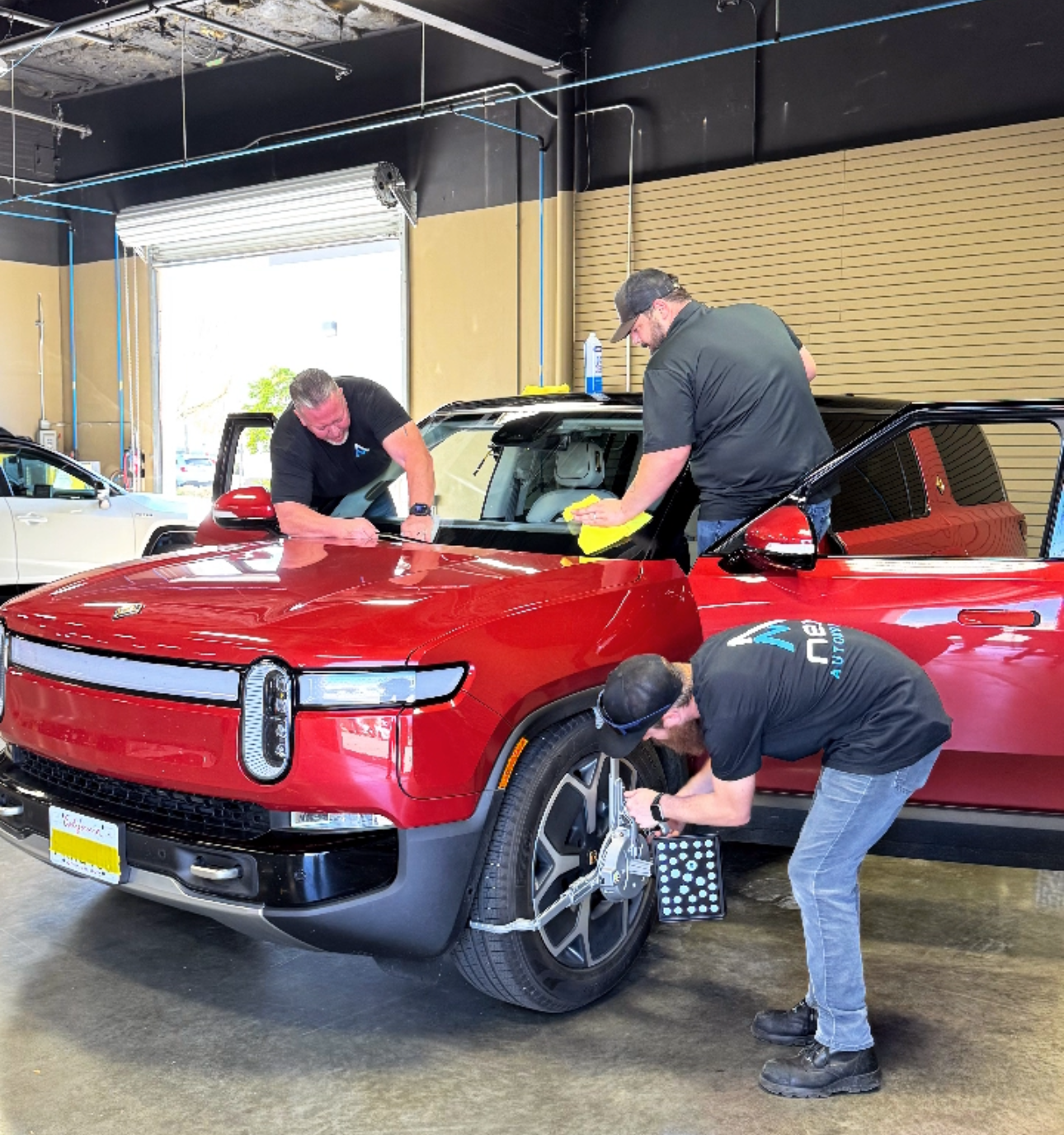 3 technicians performing auto glass replacement on a Rivian vebicle in the rocklin, ca shop